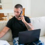 Man sitting on a couch taking notes on a notepad while on a phone call, preparing for a first recruiter conversation