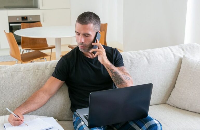 Man sitting on a couch taking notes on a notepad while on a phone call, preparing for a first recruiter conversation